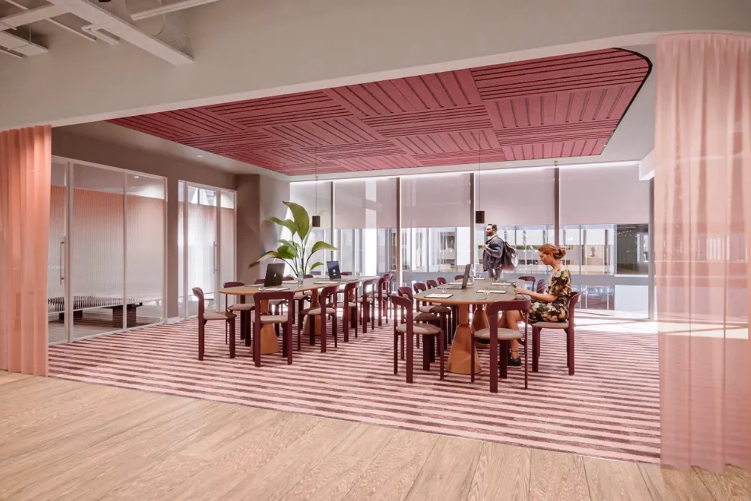Maroon chairs around two oval-shaped wooden tables on a pink-and-grey striped carpet, featuring a pink panelled ceiling section and glass-walled meeting rooms.
