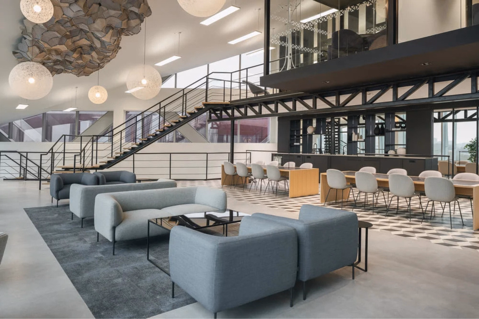 Grey armchairs and sofas on a grey rug plus wooden dining tables with white chairs on a geometric tiled floor.
