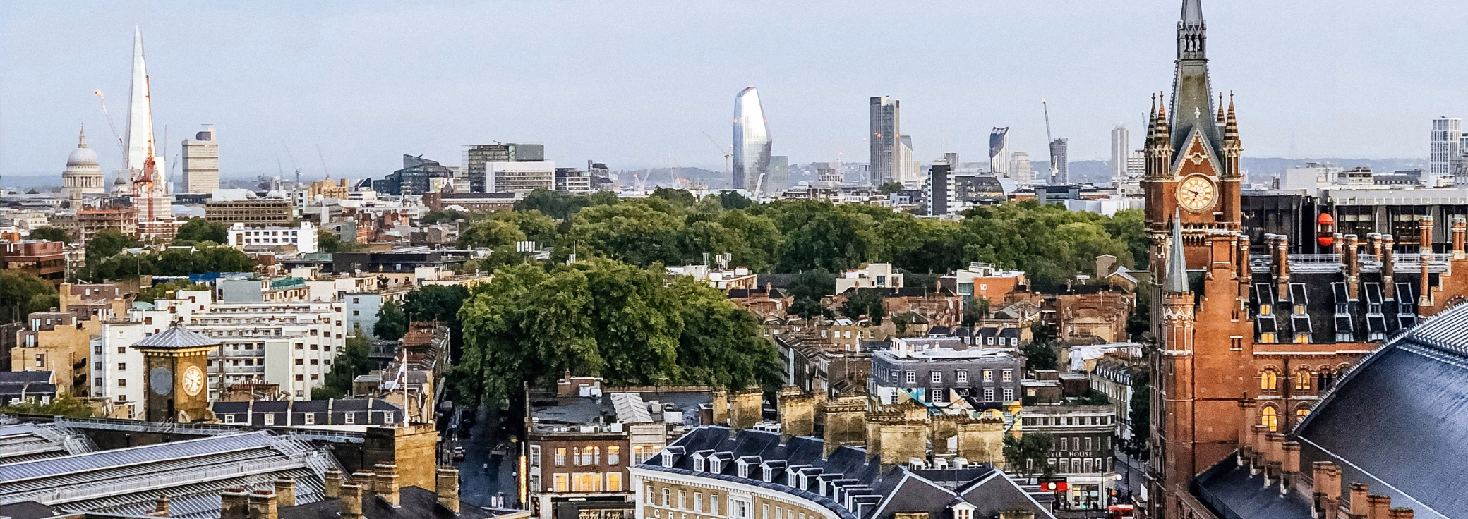 A city view features the red-brick clock tower of St Pancras International station on the right, and a distant London skyline that includes St Paul's Cathedral and The Shard.