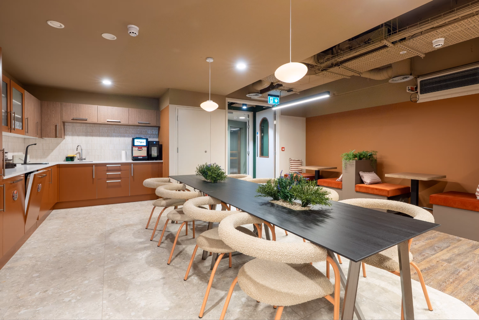 Cream-coloured chairs surround a black dining table, plus an L-shaped kitchen with brown lower cabinets and several booth seating areas.
