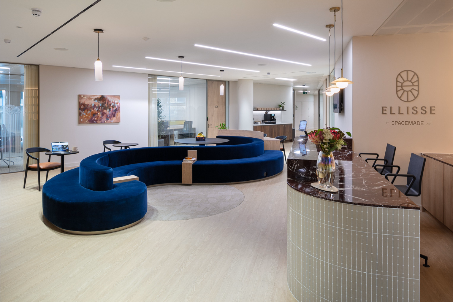 A marble reception desk beside a large blue velvet sectional sofa, featuring light wood floors and a wall displaying the "ELLISSE by SPACEMADE" logo.