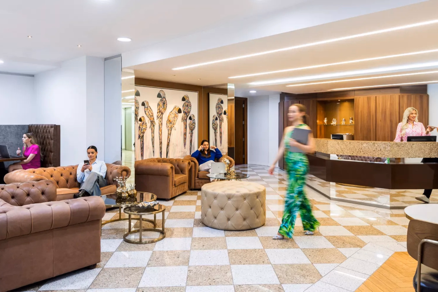 Brown leather sofas and armchairs in a reception and lounge area featuring a tan-and-white checkered floor and a wooden reception desk.