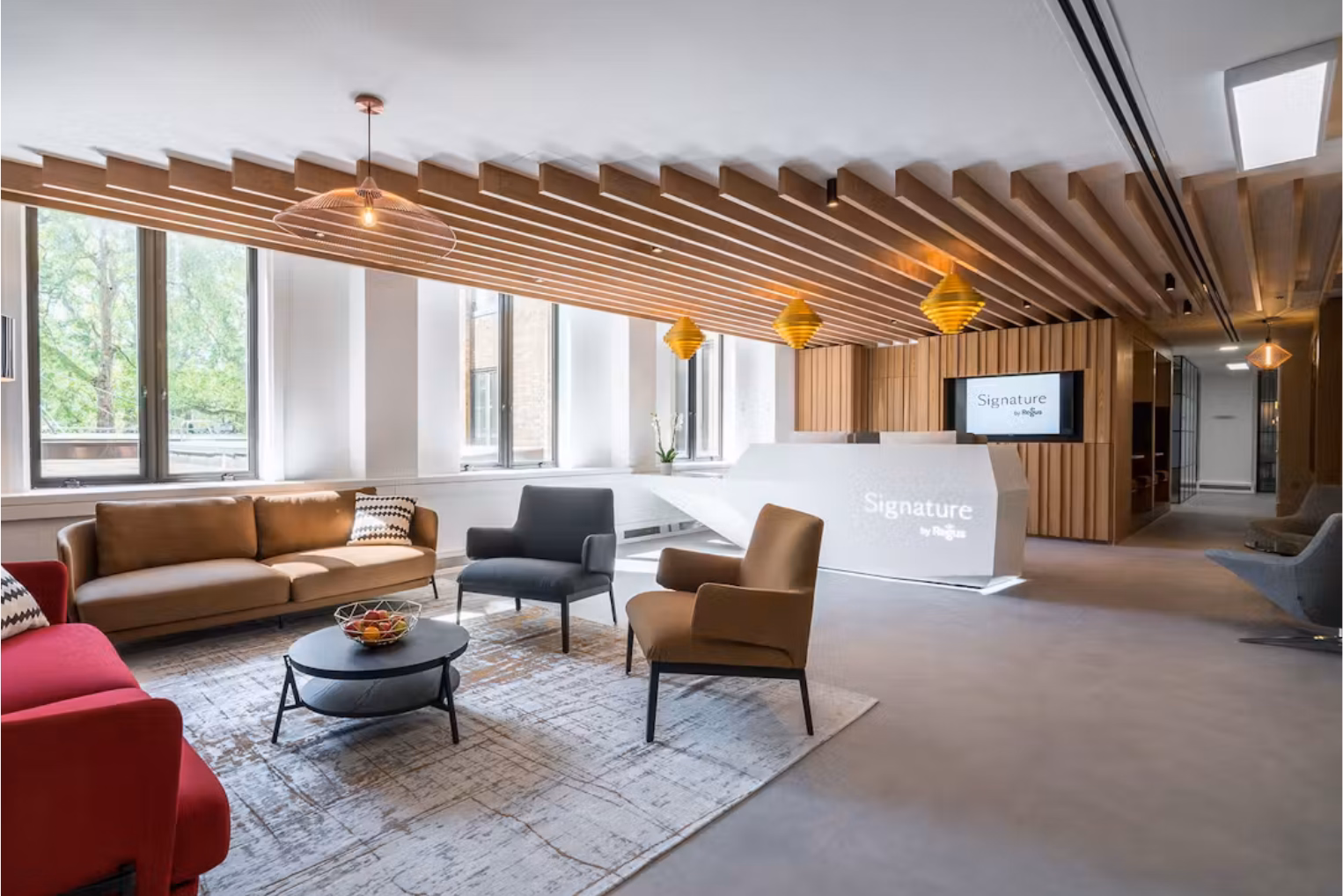 A white reception desk bearing the "Signature by Regus" logo under a slatted wood ceiling, next to a lounge area featuring various sofas and a table.