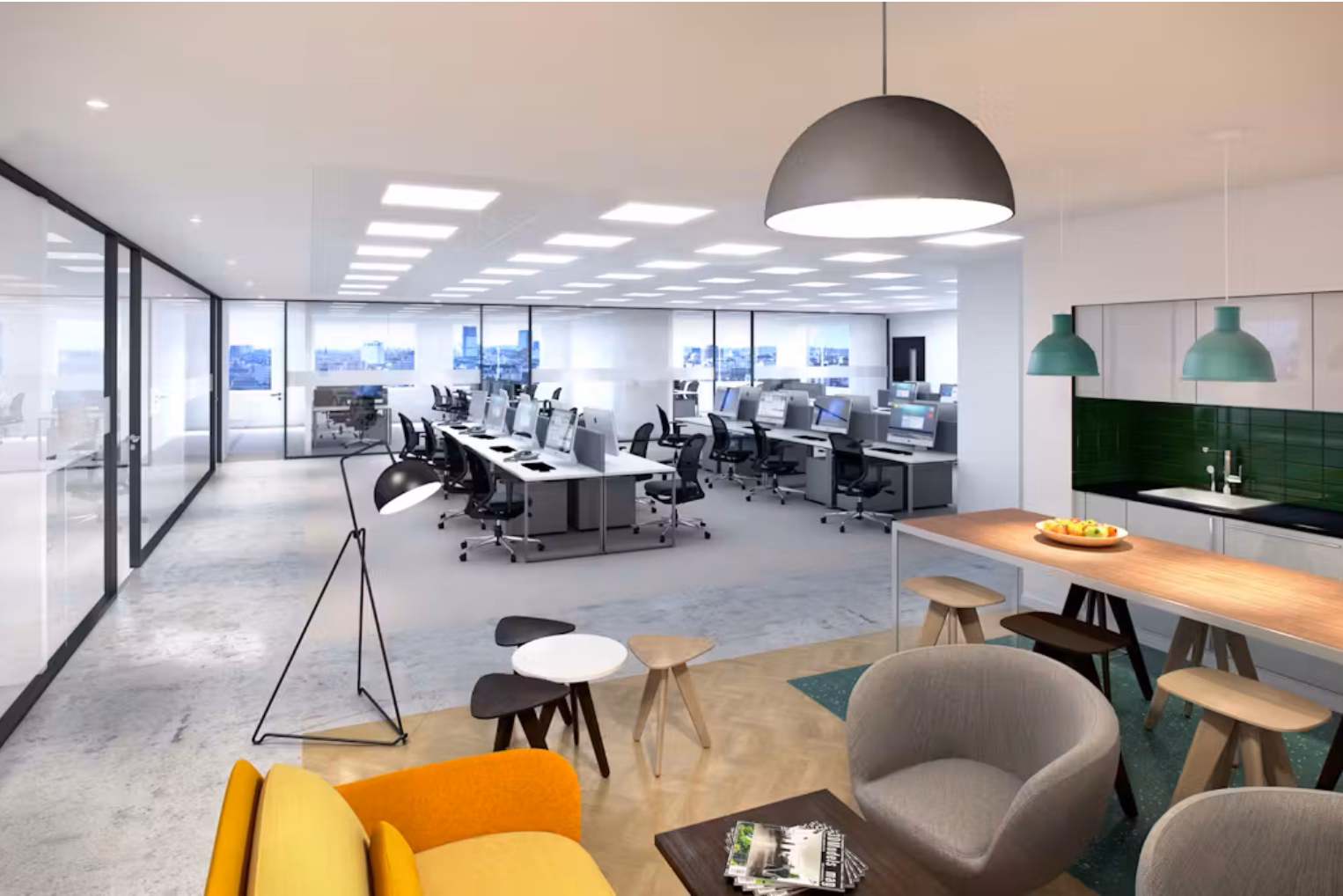 An open-plan office features rows of white desks with desktops stretching into the background, bordered by a kitchen area with a wooden breakfast bar and stools.