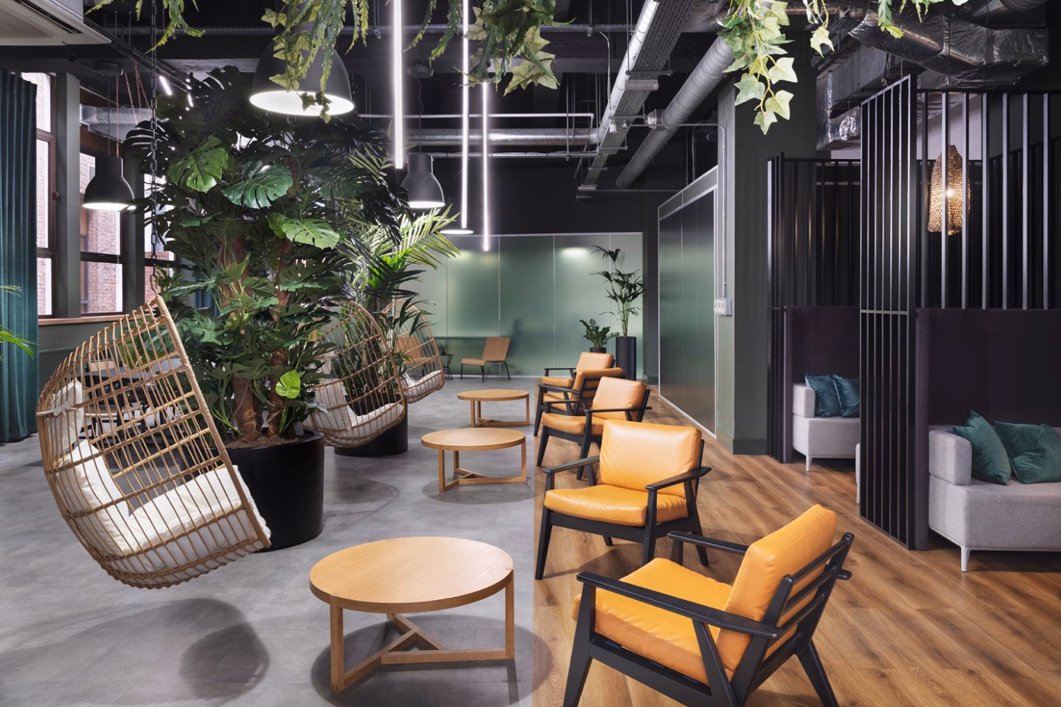 Woven hanging egg chairs with white cushions and tan leather armchairs around round wood coffee tables in a biophilic office lounge.