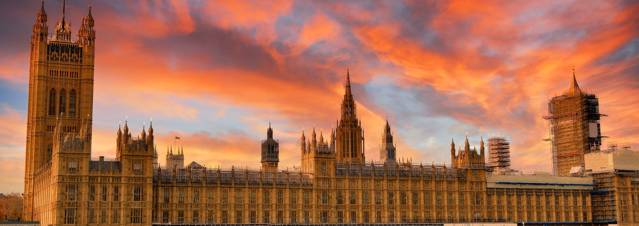 The Palace of Westminster silhouetted against a sunset sky filled with vibrant orange, pink, and purple clouds.