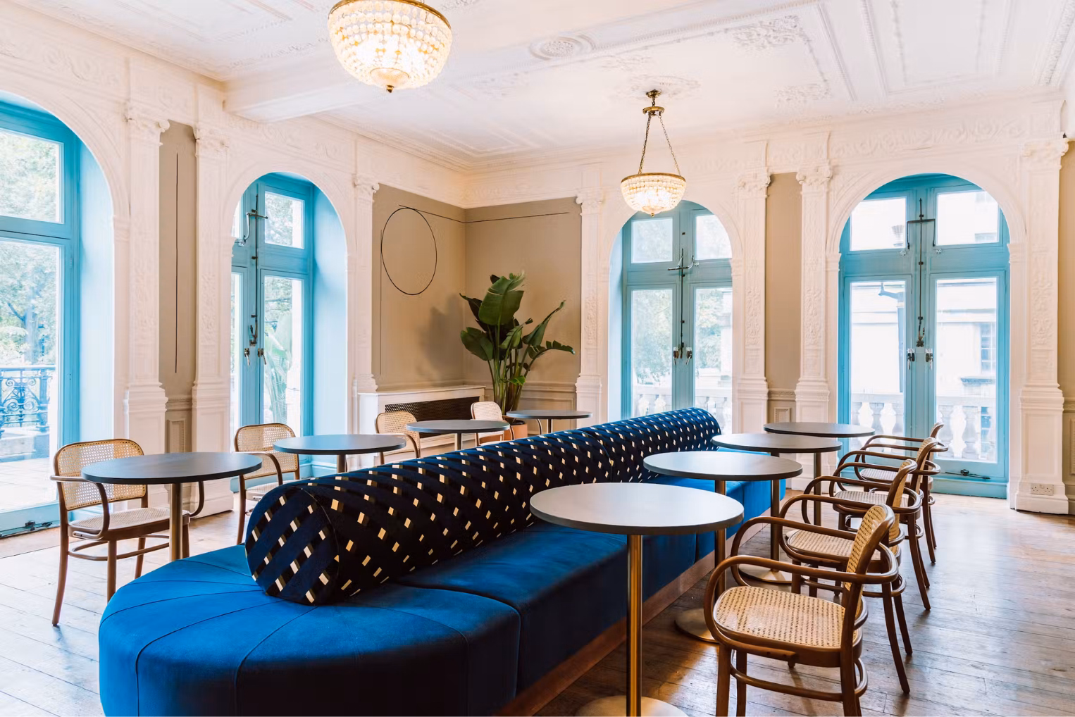 Woven-seat chairs surround round tables set along a long, double-sided banquette featuring a patterned bolster cushion.