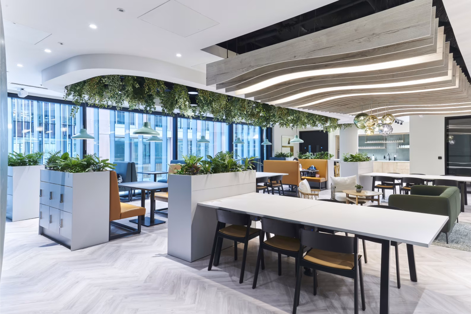Black chairs along a long white worktable feature built-in planters with greenery and booth seating options.