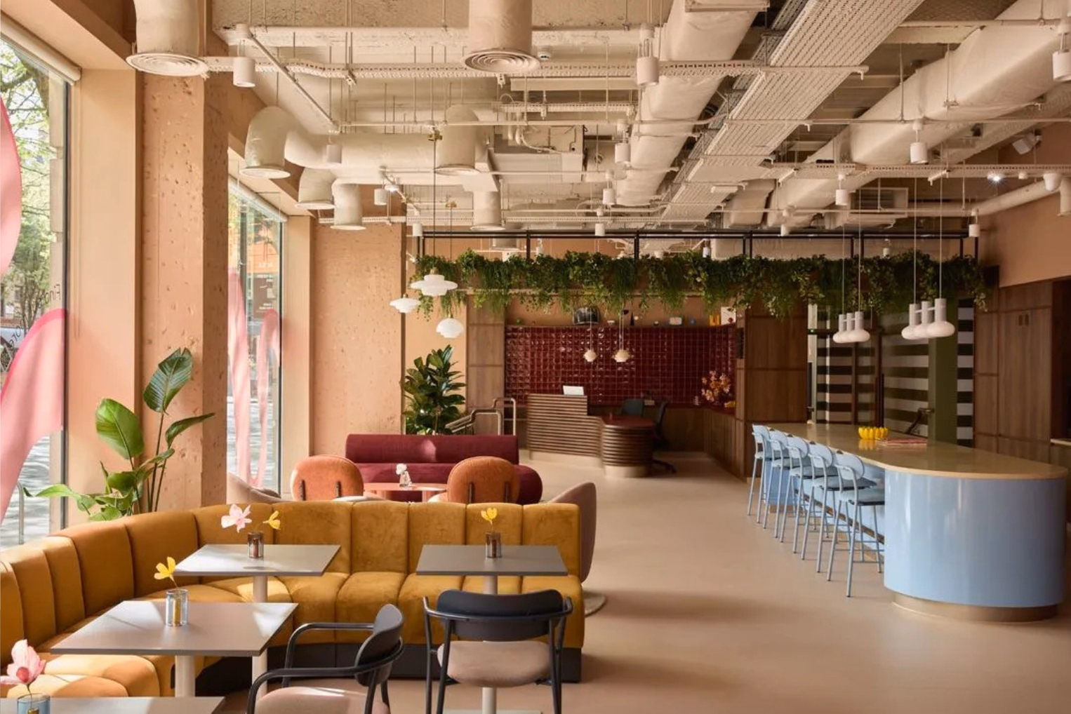 An office lounge features a curved yellow banquette sofa with square tables, a light blue island bar paired with light blue barstools.
