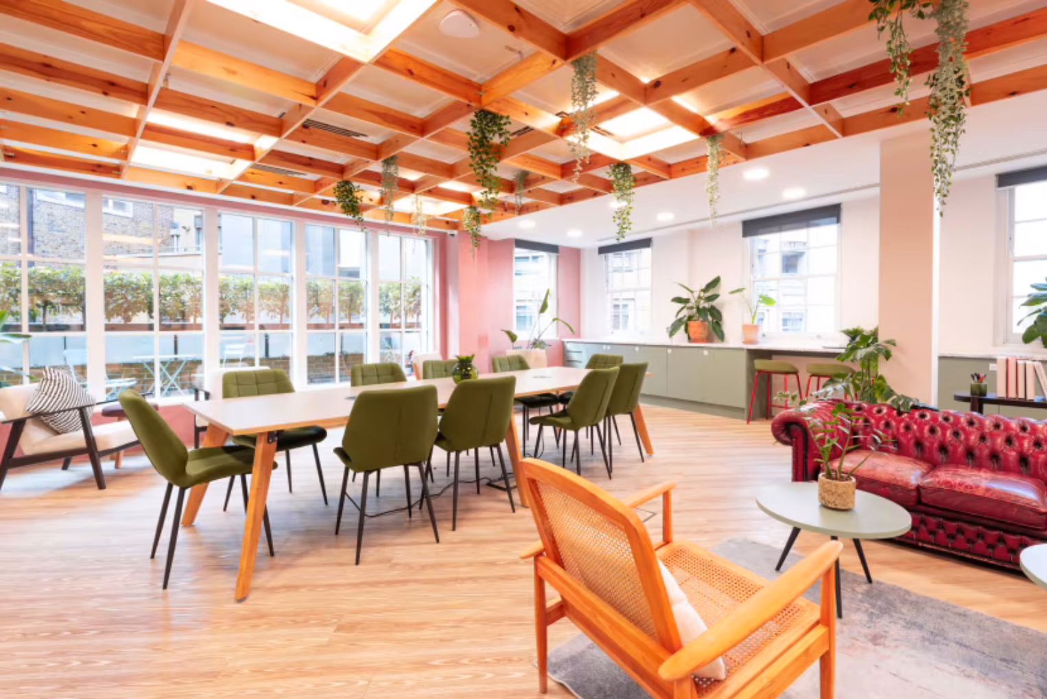Olive green chairs surround a long table in a bright office space that features a wooden grid ceiling with hanging trailing plants.