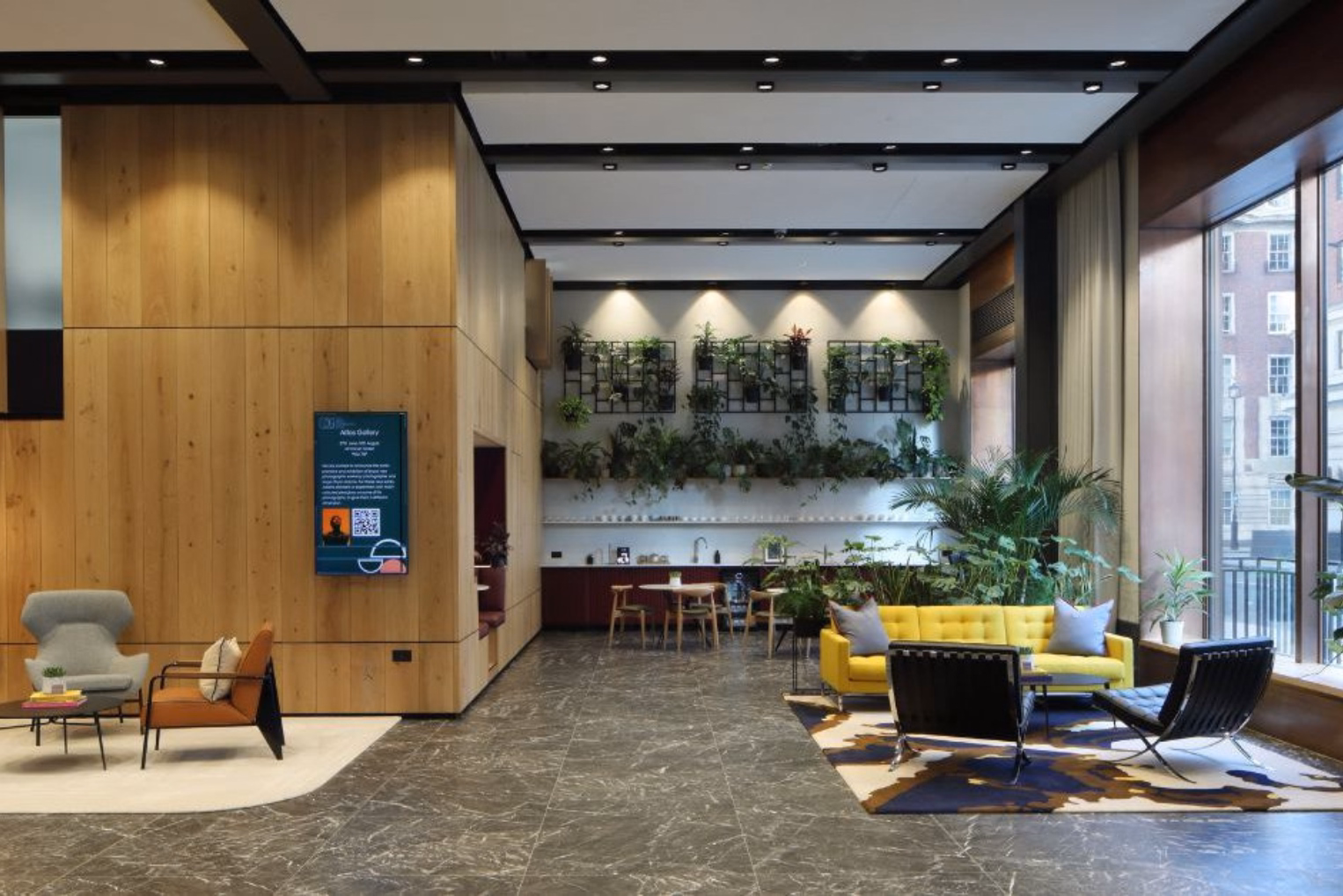 A bright yellow sofa and black leather chairs on a patterned area rug, high-ceiling office lobby featuring dark marble flooring and warm wood-panelled walls.