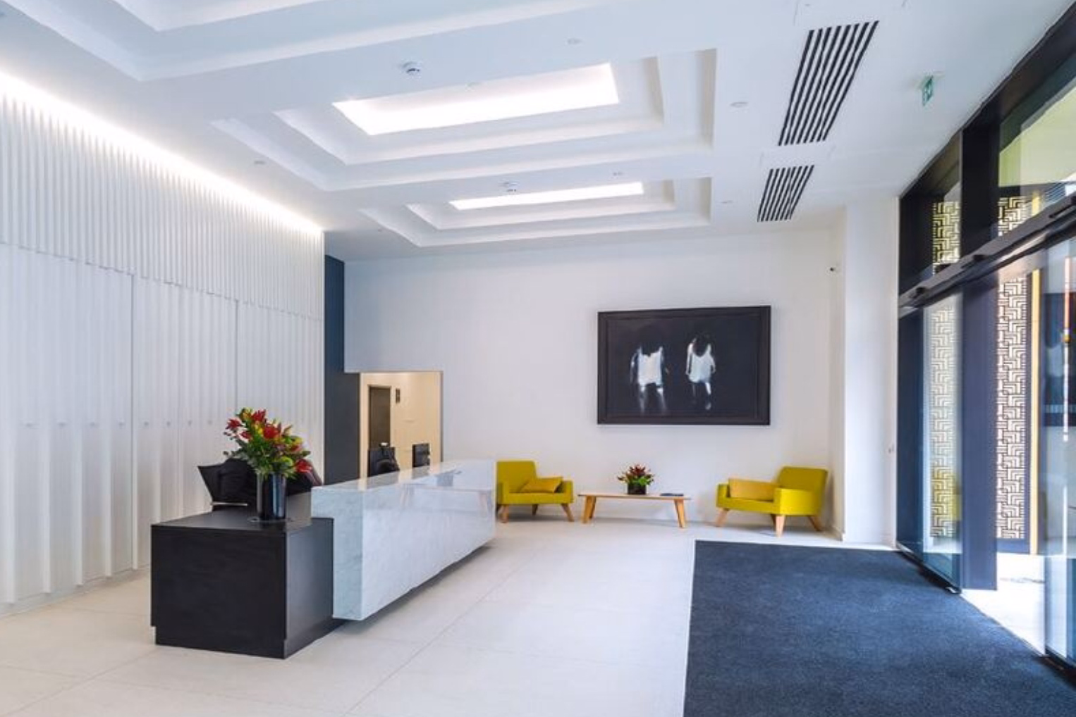 Green armchairs surround a wooden table in a reception area, featuring a black and white marble reception desk, vertical wall panelling, and dark framed artwork.