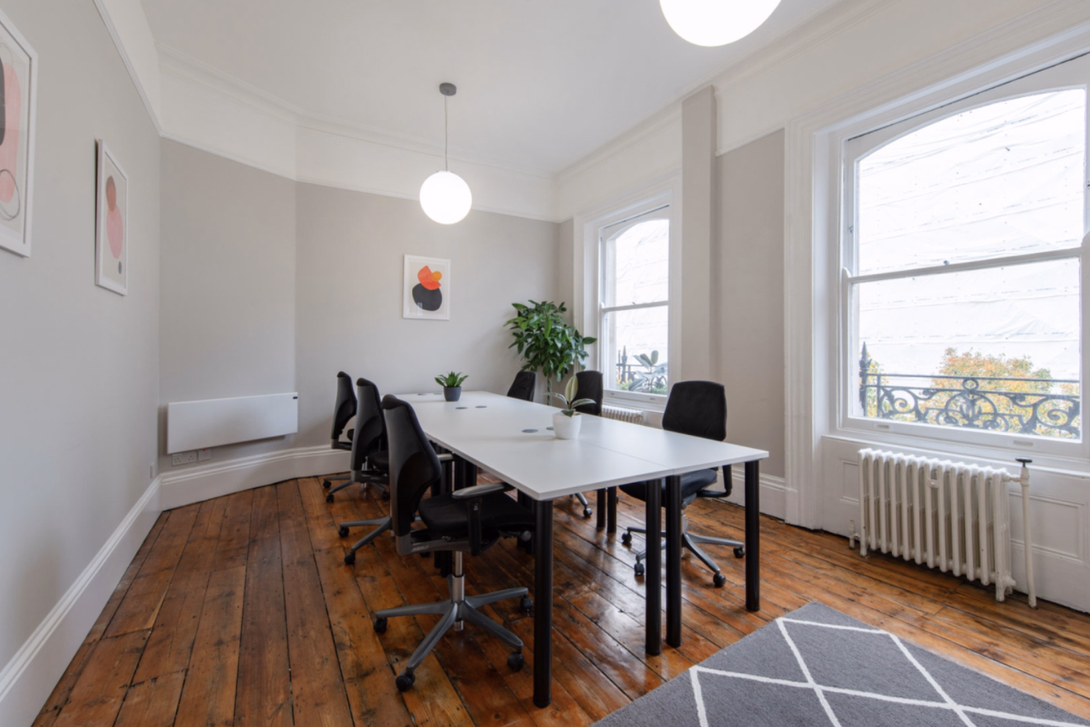 Black chairs surround a white table in a bright room featuring wooden floorboards, large white-framed windows and spherical pendant lights.