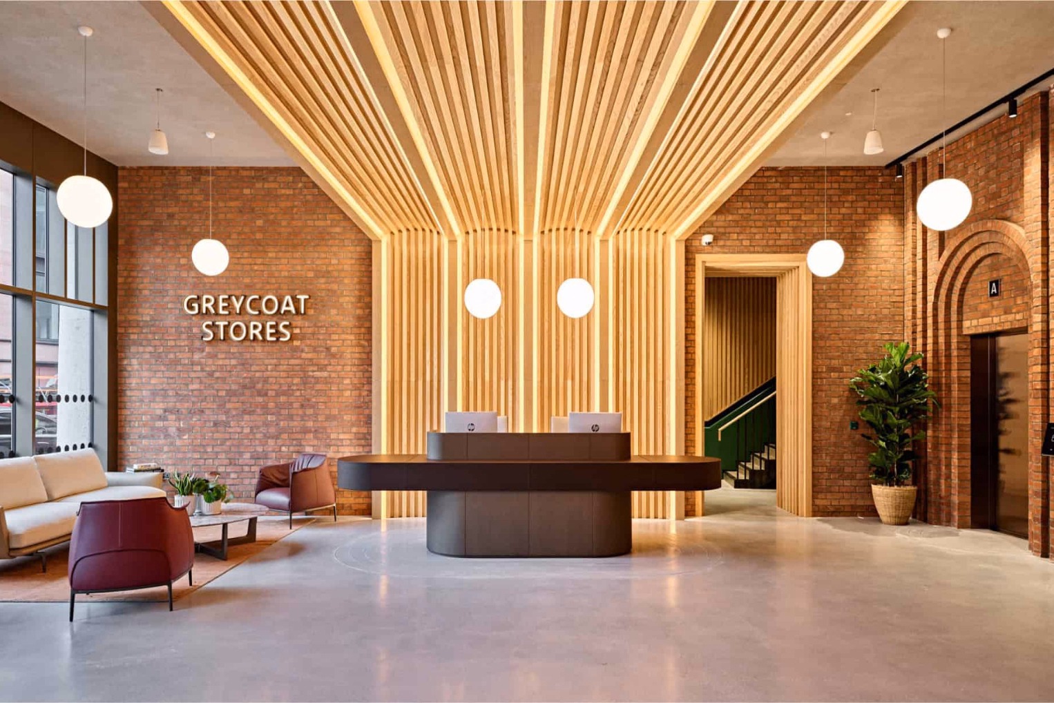 A reception desk centrally beneath a canopy of back-lit vertical slats that extend to the ceiling in an office waiting area, with a "GREYCOAT STORES" sign on the wall.