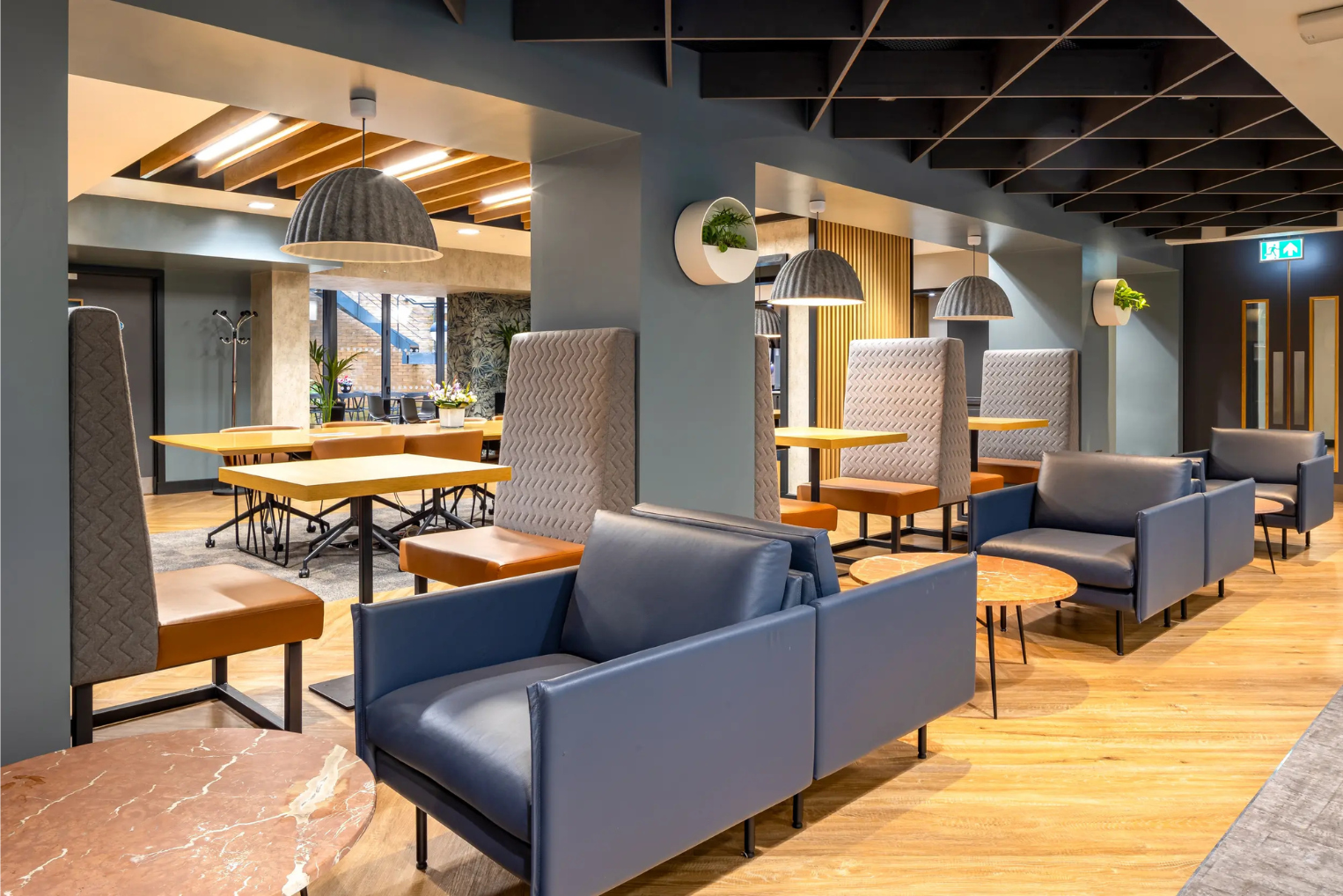 A office lounge featuring blue leather armchairs and high-backed privacy booths on light wooden flooring.