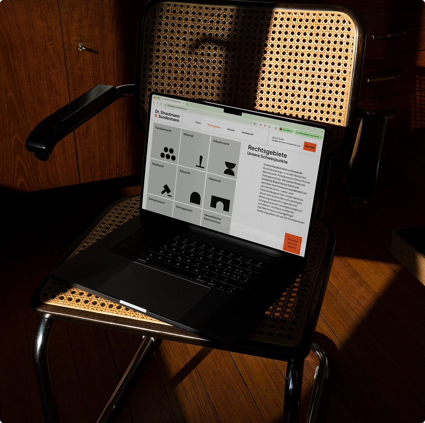 Laptop on a wooden chair displaying the website of the law firm Dr. Strautmann & Sundermann. The page shows different areas of legal practice represented with bold black icons, alongside a text section titled “Rechtsgebiete – Unsere Schwerpunkte.”