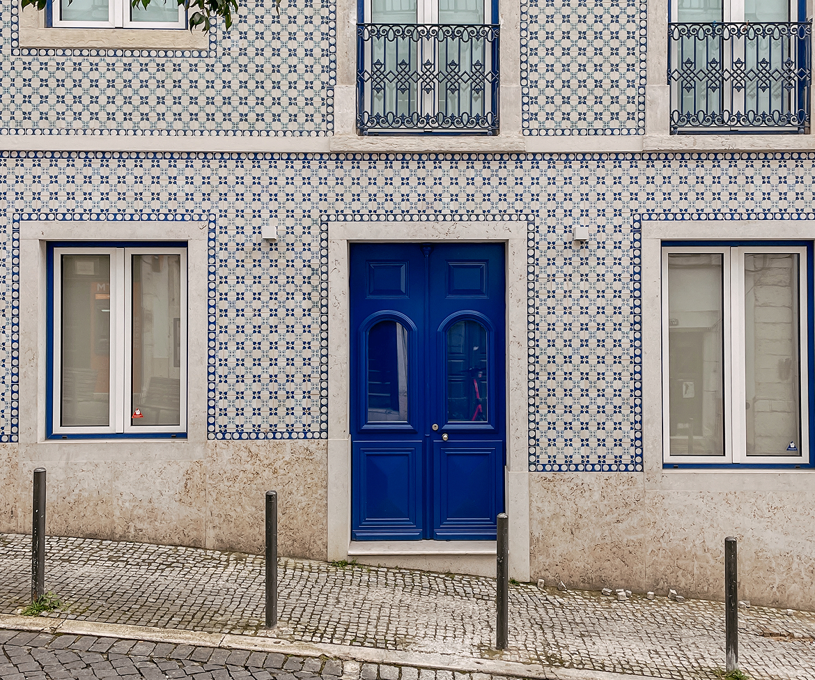 Facade of a house with blue patterned tiles, blue framed windows, and a blue double door in Lisbon.
