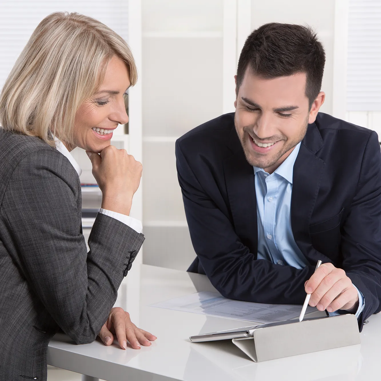 Ein Mann und eine Frau in Geschäftskleidung sitzen an einem Tisch, der Mann zeigt der Frau die Filialverwaltung in der Bestattersoftware Rapid Next auf einem Tablet.