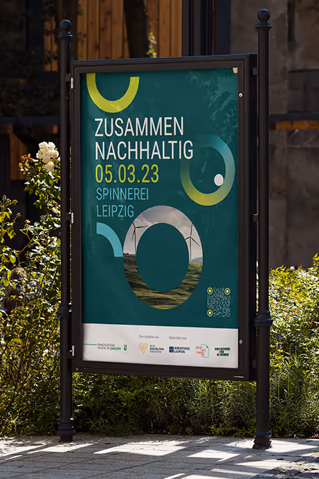 Outdoor signboard with green background advertising a sustainability event in Leipzig on 05.03.23 with circular graphic elements and wind turbines image.