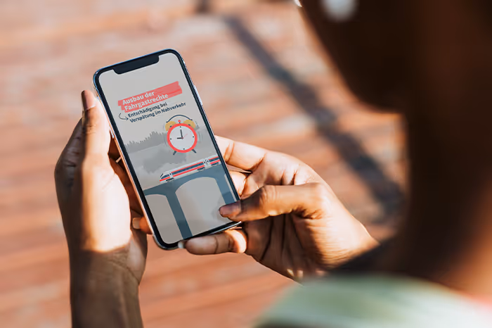 Person holding smartphone displaying a graphic of a train on a bridge with a clock and German text about expanding railways and improving local transport.