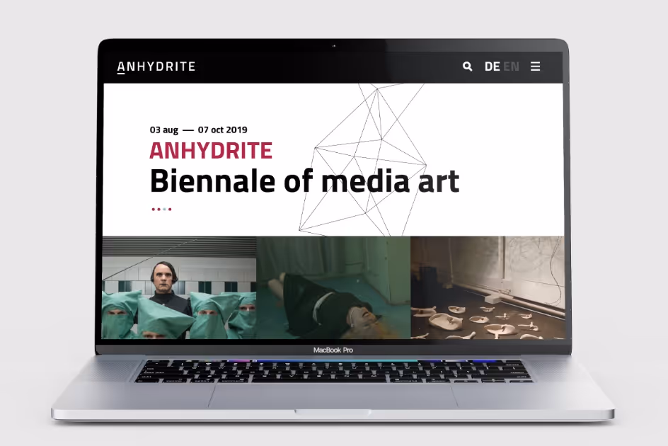 MacBook Pro screen displaying the Anhydrate Biennale of media art event dated 03 Aug to 07 Oct 2019, with images of people in green surgical attire, a person lying down, and pottery pieces.