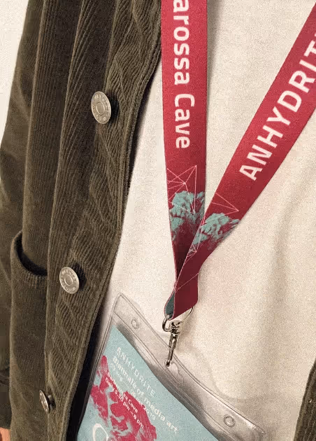 Person wearing a brown corduroy jacket and white shirt with a red lanyard that reads 'Narossa Cave Anhydrite' holding a badge in a clear plastic holder.
