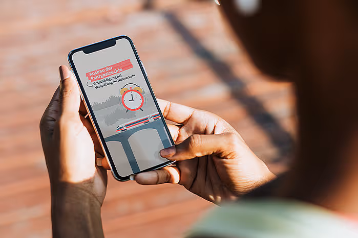 Person holding a smartphone displaying an app screen with a clock and a train on a bridge illustration.