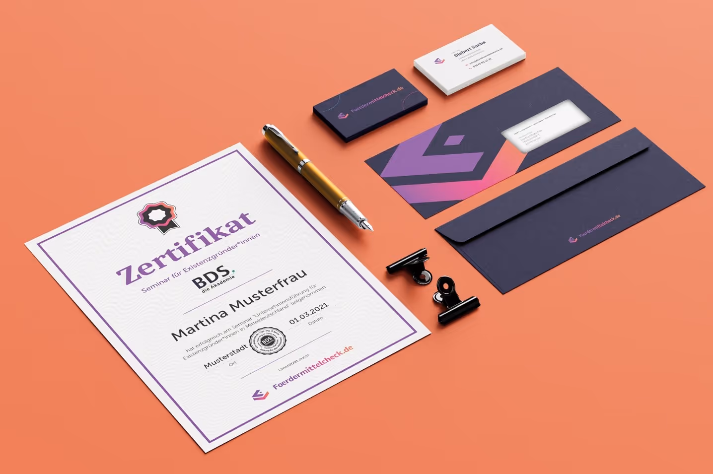 Certificate, gold pen, business cards, envelope, and binder clips arranged on an orange surface.