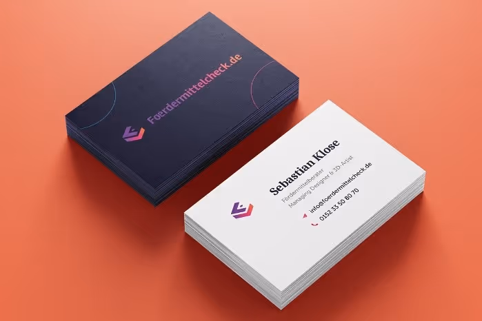 Two stacks of business cards on an orange surface, one showing the dark back with Fördermittelcheck.de logo, the other showing the front with contact details for Sebastian Klose, including email and phone number.