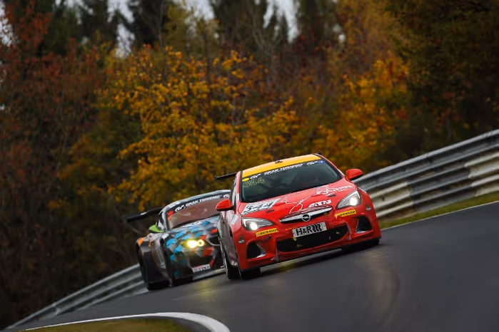Two race cars speeding on a curved racetrack surrounded by autumn trees.