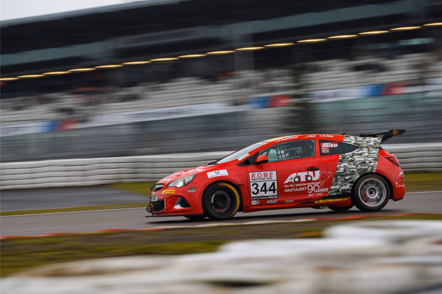 Red race car number 344 speeding on a racetrack with blurred background.