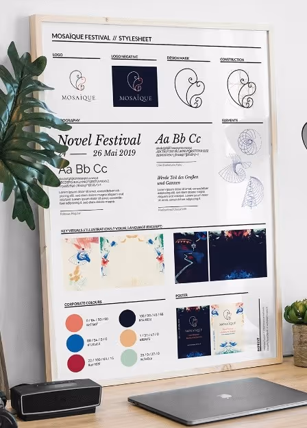 Framed style guide for Mosaique Festival on desk showing logo variations, typography, design elements, colors, visuals, and posters.