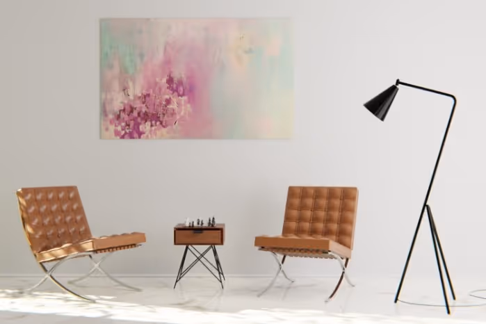 Minimalist living room with two brown leather chairs, a small table holding a chess set, a colorful abstract wall painting, and a black floor lamp.