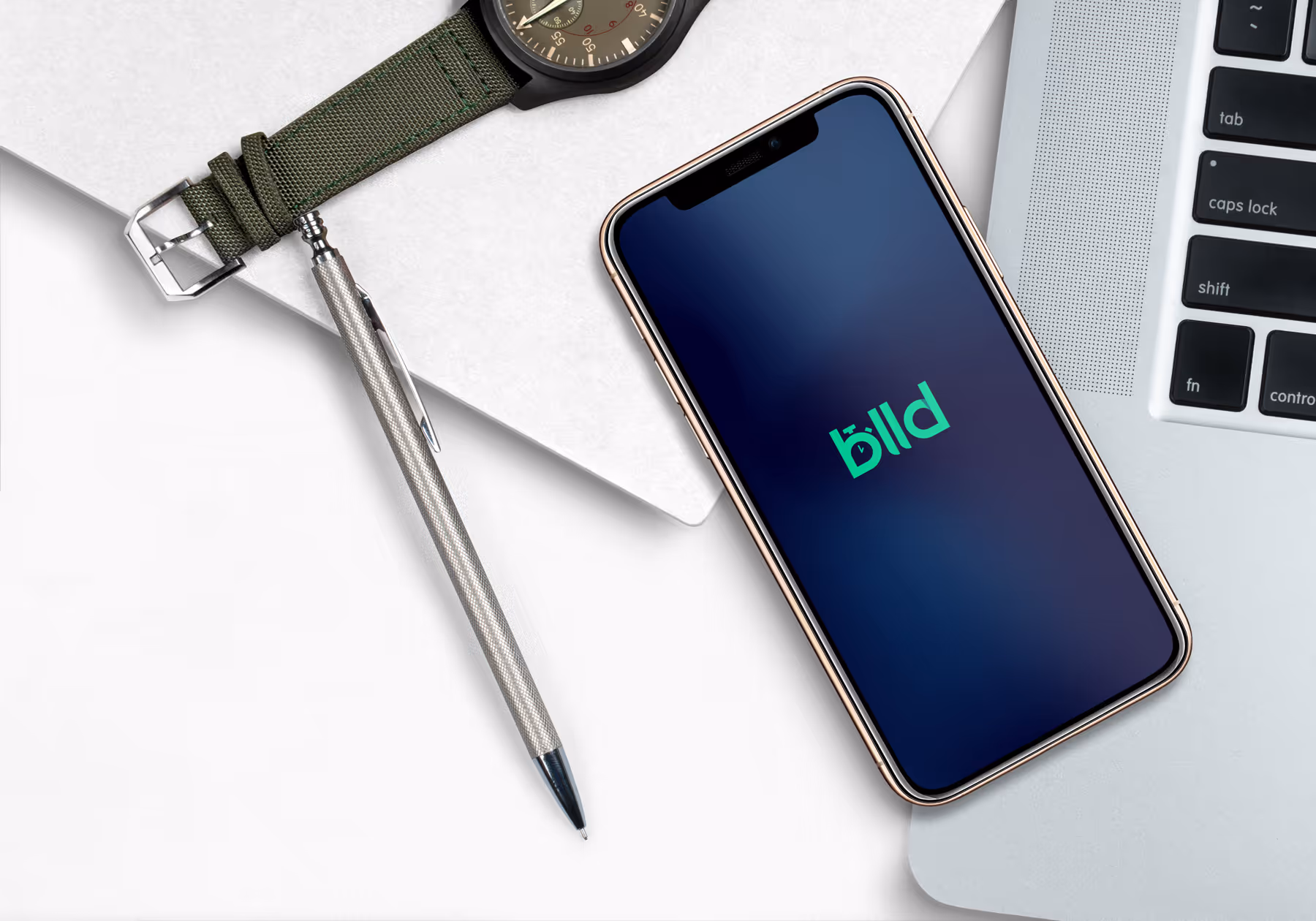 Smartphone displaying the bllld app logo placed next to a silver pen, a green wristwatch, and a laptop keyboard.