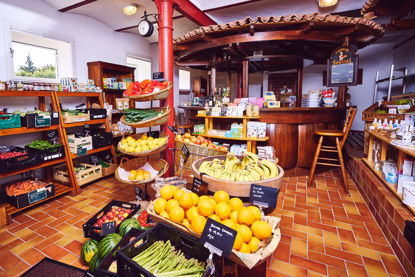 Interior of a small grocery store with fresh fruits, vegetables, and packaged goods displayed on wooden shelves and baskets.