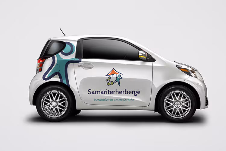 White compact car with Samariterherberge logo and slogan 'Herzlichkeit ist unsere Sprache' on the door and a stylized graphic of people on the rear side panel.