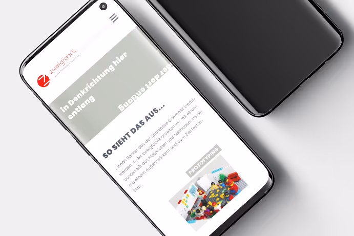 Smartphone displaying a webpage with text and an image of colorful LEGO bricks labeled 'PROTOTYPING', next to a black smartphone on a white surface.