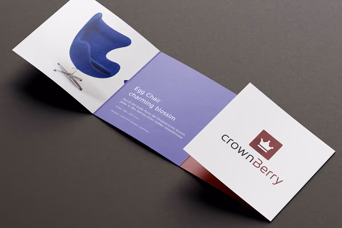 Open tri-fold brochure on gray surface displaying a blue Egg Chair on the left, purple middle panel with text about the chair, and CrownBerry logo on the right panel.