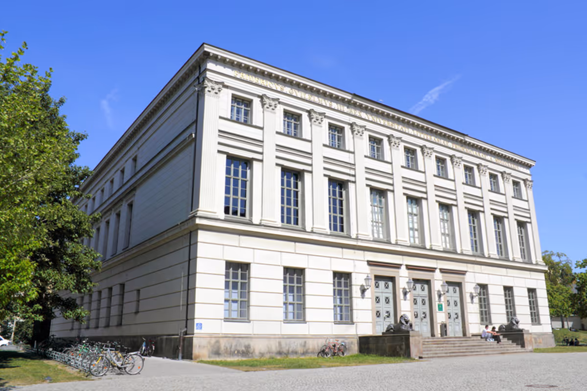 Large white neoclassical building with tall windows, columns, and stairs flanked by lion statues under a clear blue sky.