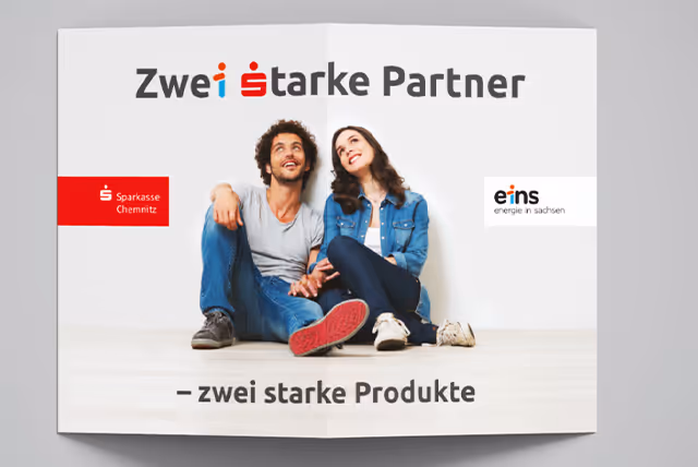 Smiling young couple sitting on the floor holding hands under the text 'Zwei starke Partner – zwei starke Produkte' with logos of Sparkasse Chemnitz and eins energie in sachsen.