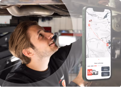 Mitarbeiter blickt lächelnd unter ein angehobenes Fahrzeug, daneben ein Smartphone mit Kartenansicht und Live-Tracking der FleetHub-App.