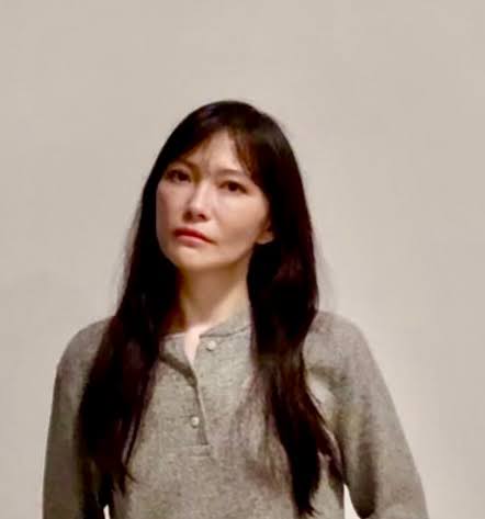 Woman with long dark hair wearing a gray buttoned sweater against a light background.