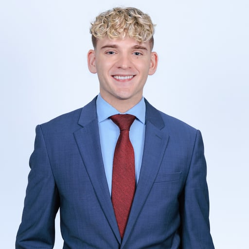 Smiling young man with curly blond hair wearing a blue suit, light blue shirt, and red tie.