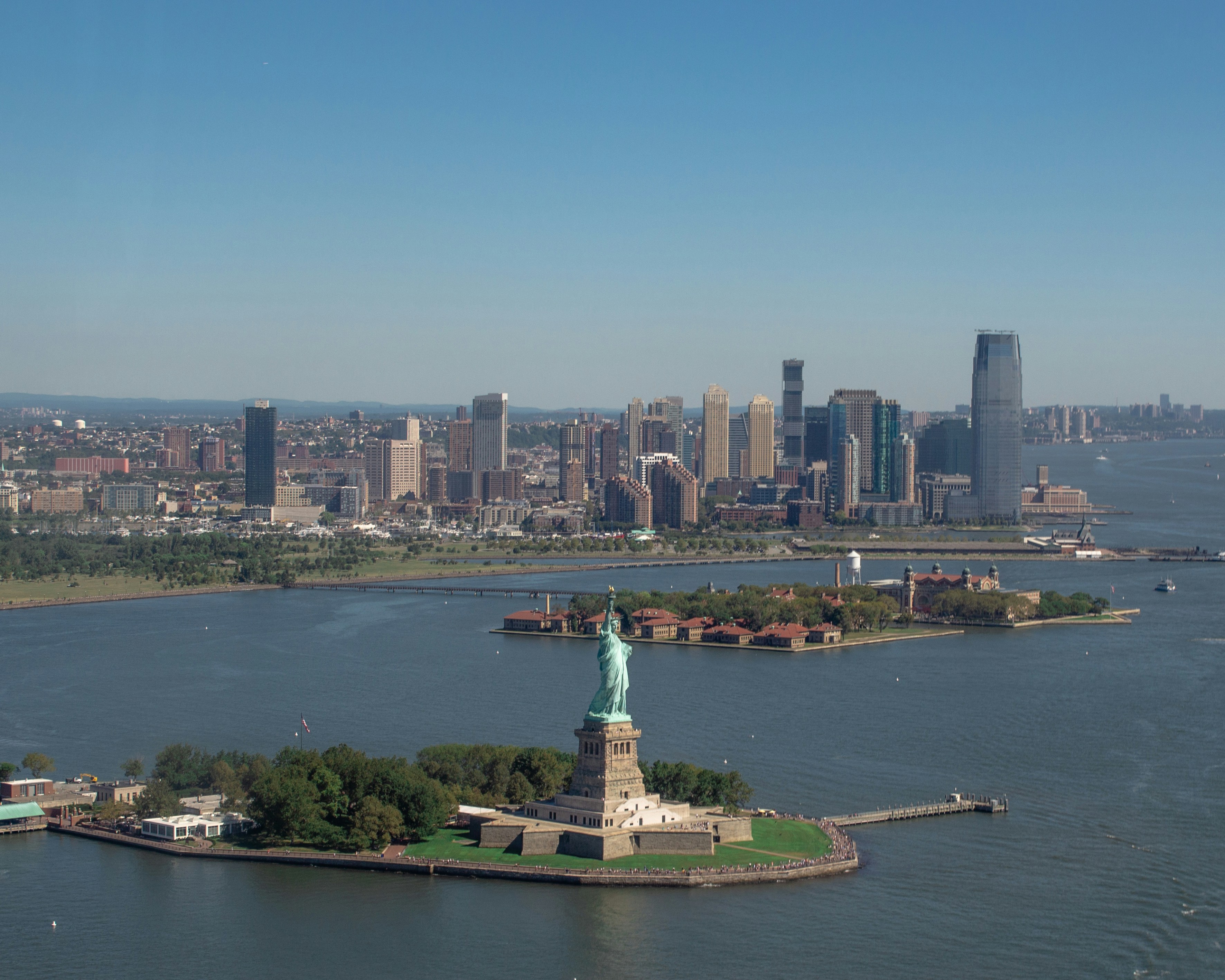Aerial view of the Statue of Liberty on Liberty Island with Manhattan skyline in the background.