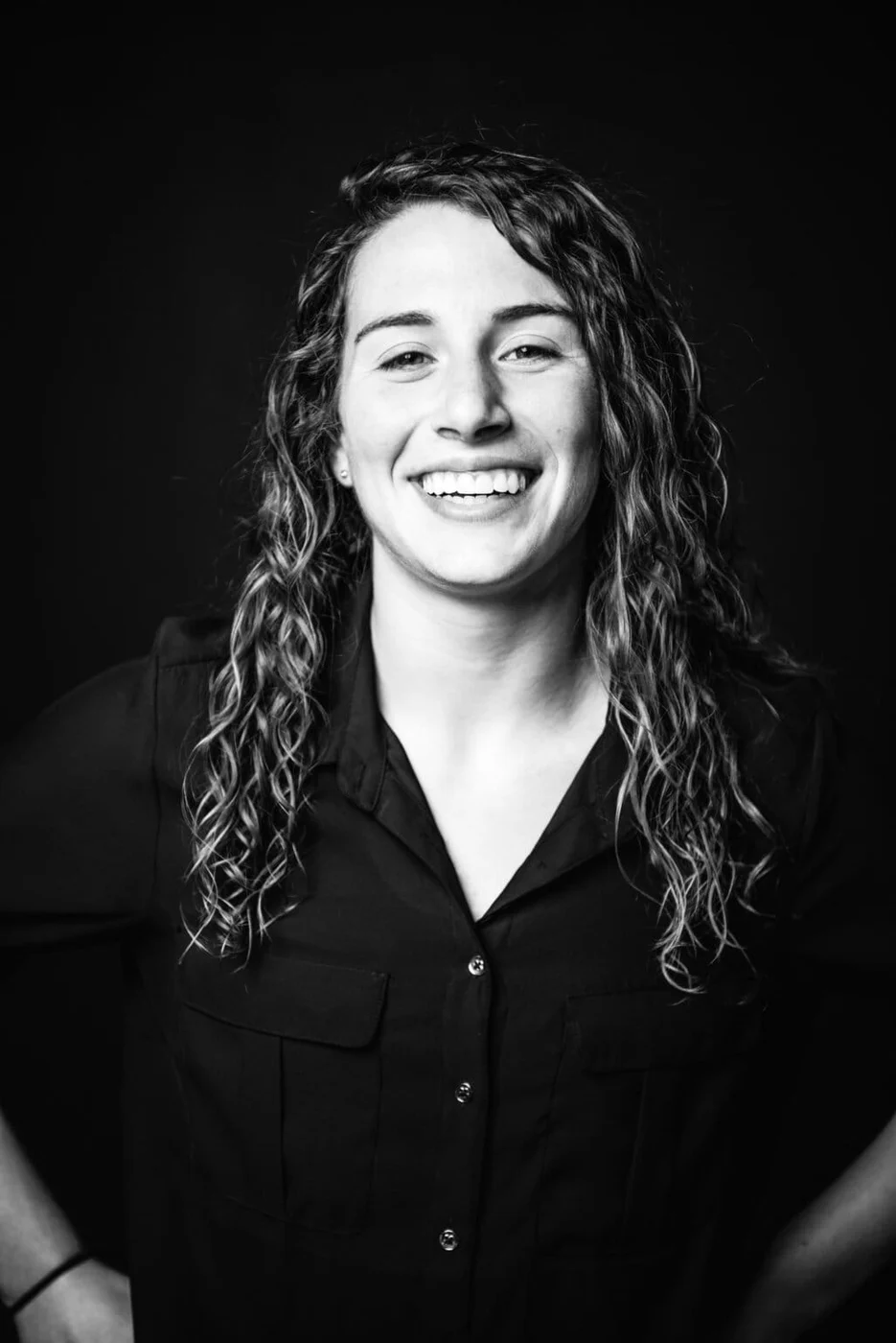 Retrato en blanco y negro de una mujer sonriente con cabello rizado, vistiendo una camisa oscura de botones.