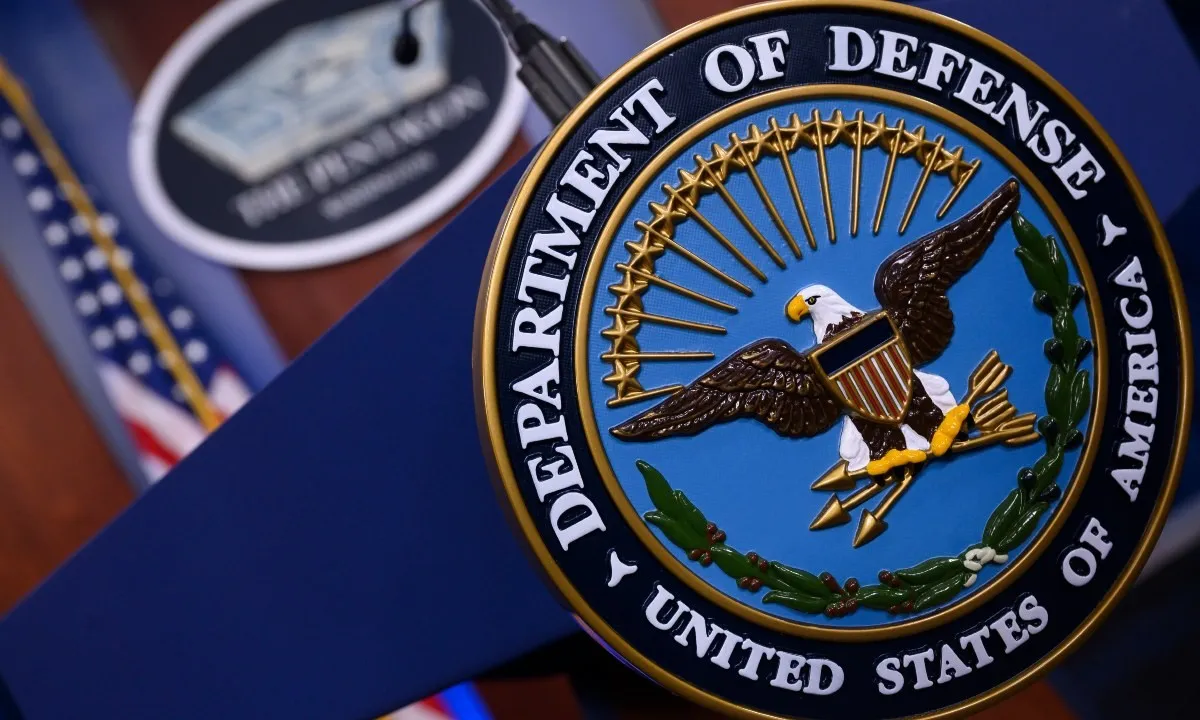 Seal of the United States Department of Defense displayed on a podium, with the Pentagon emblem and American flags in the background.
