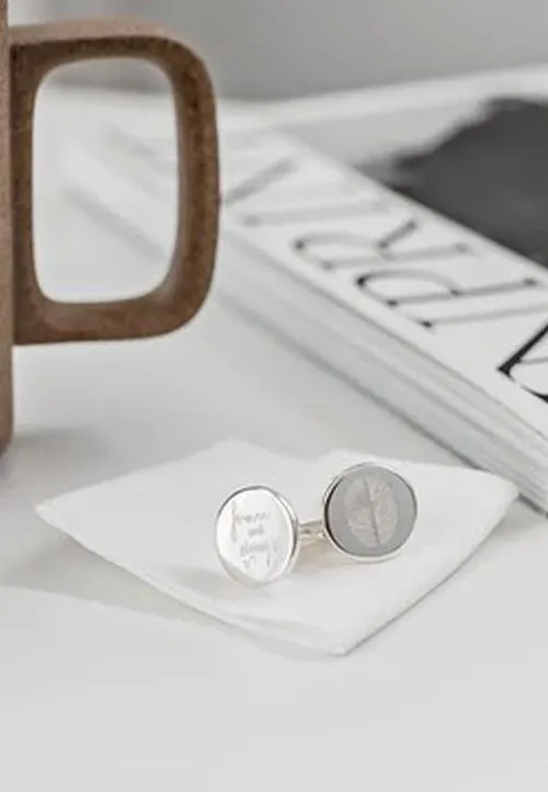 Silver cufflinks resting on a white cloth with a brown mug handle and a book in the background.