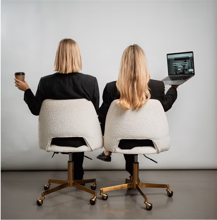 two women sitting in chairs with a laptop and a cup of coffee