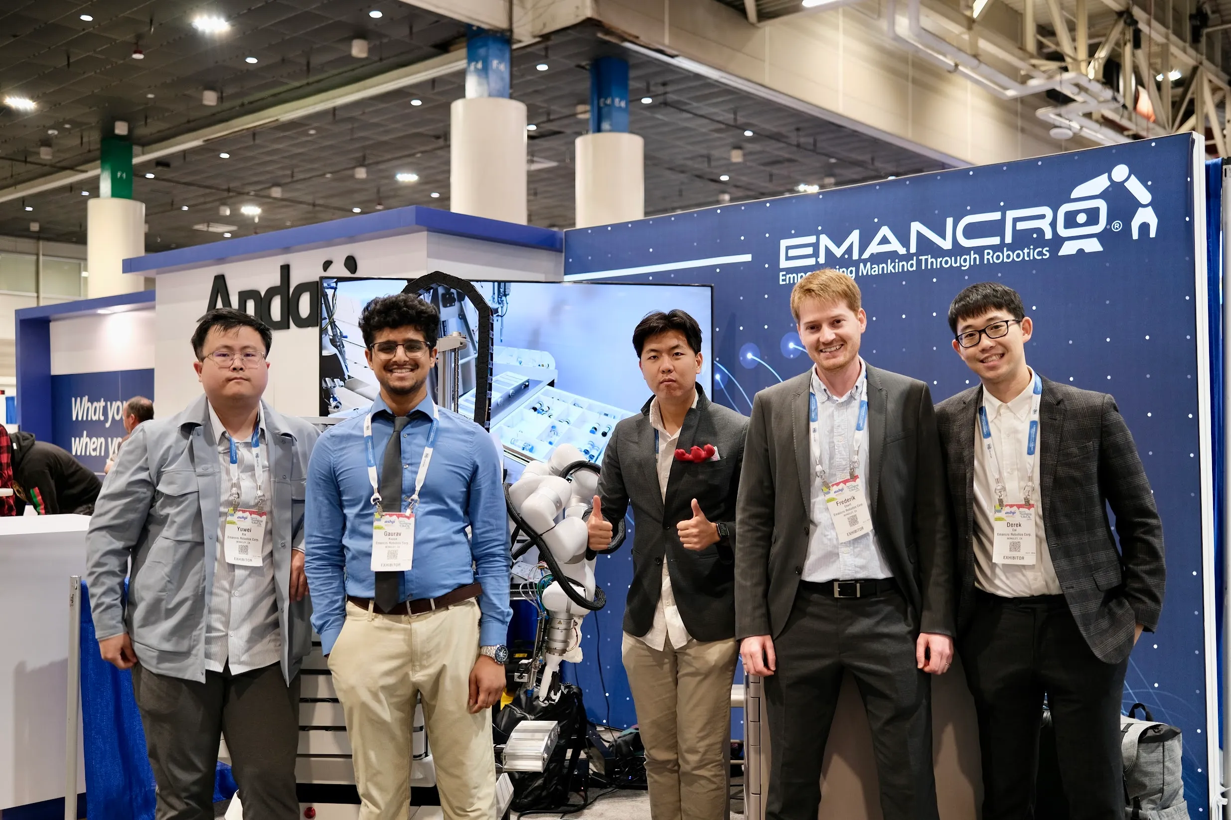 Emancro team posing at a healthcare technology exhibition booth with their dual-arm medical robot and company branding in the background.