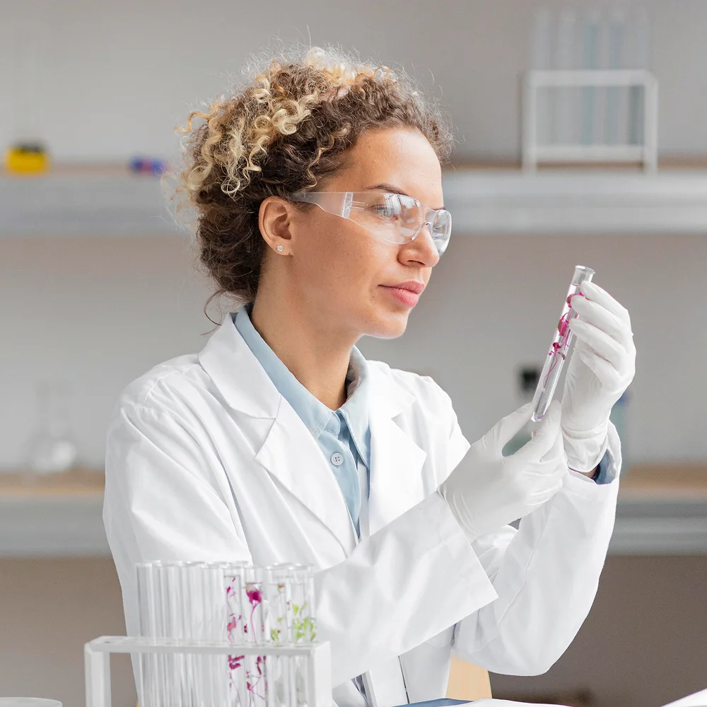 Female scientist wearing protective goggles examines a test tube with samples, showcasing modern laboratory research and innovation in healthcare.